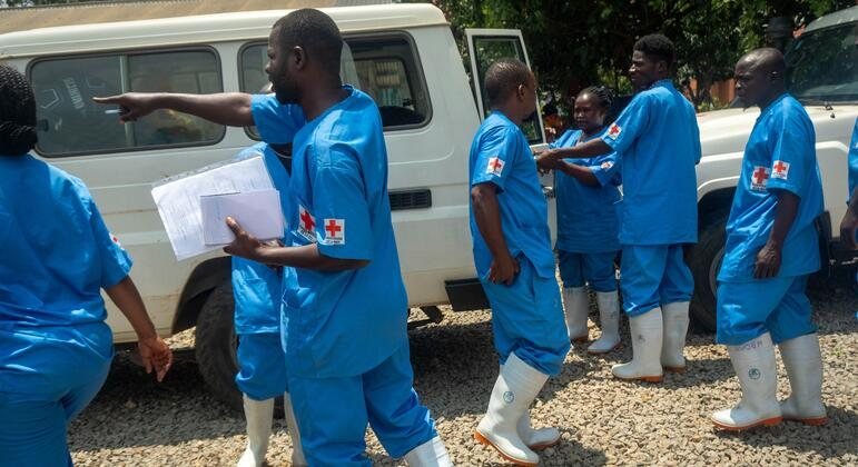 Personal de salud con uniformes azules y botas blancas conversan frente a un vehículo en una zona rural
