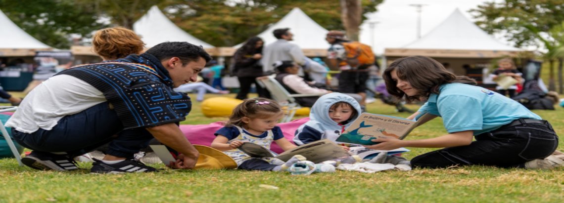 Una familia con dos niños pequeños juega en el césped durante un evento al aire libre con carpas blancas.