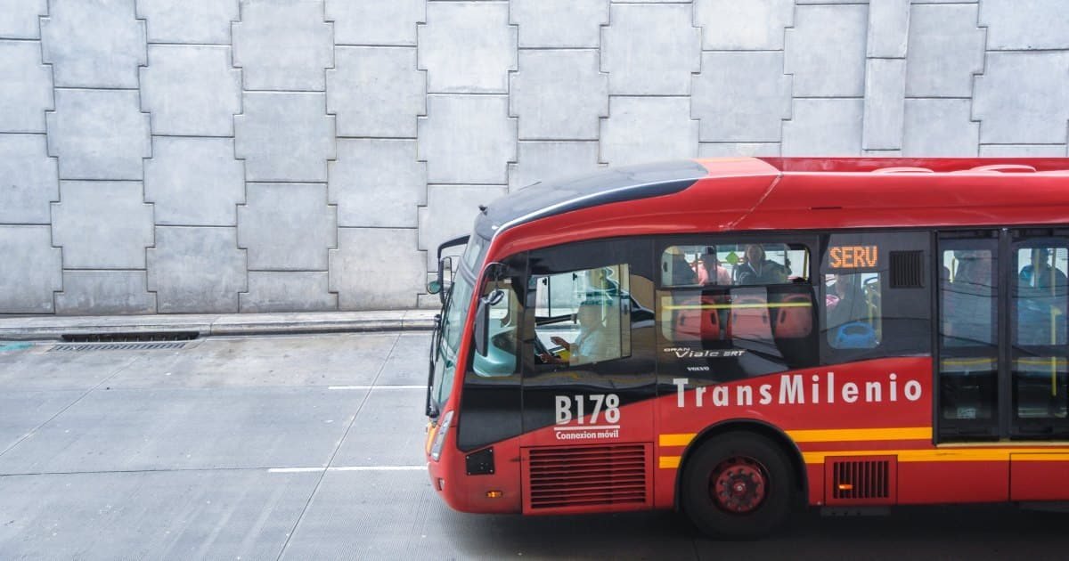 Un autobús rojo de TransMilenio circula por una calle frente a una pared de bloques grises.