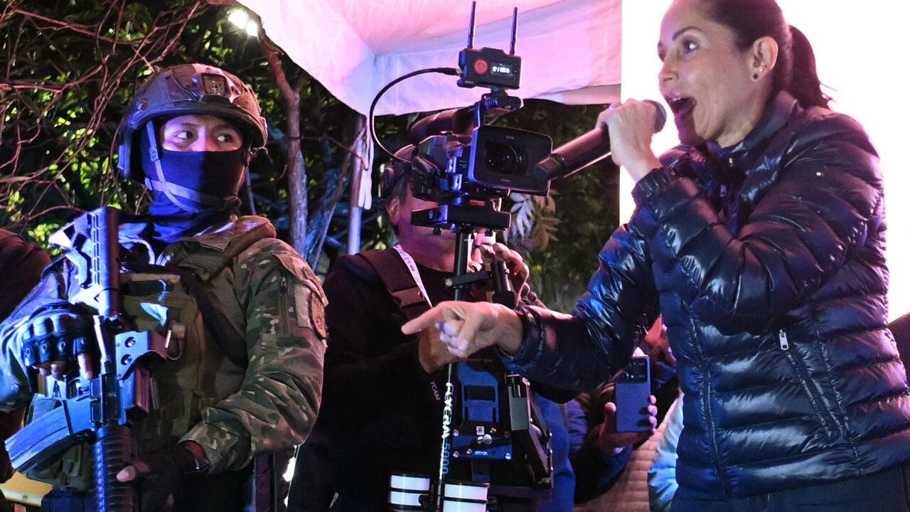 Una mujer con un micrófono habla frente a un operativo policial con agentes uniformados y armados en la noche