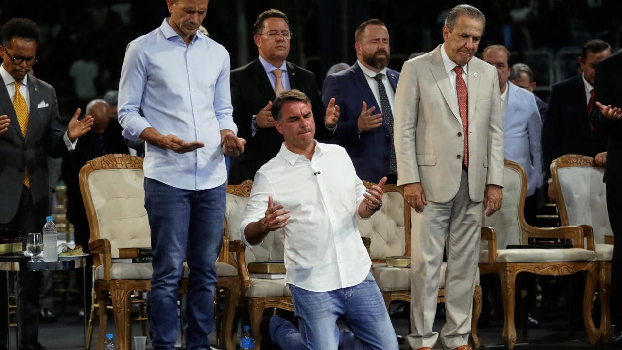 Un hombre arrodillado con las manos extendidas frente a un grupo de hombres en un escenario