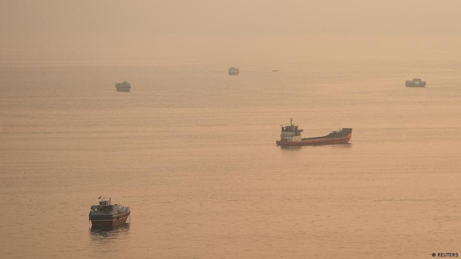 Varios buques cisterna navegan en un mar brumoso bajo una luz anaranjada