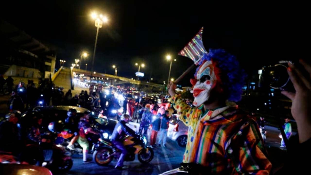 Una persona disfrazada de payaso en una calle de noche con motociclistas y luces de ciudad