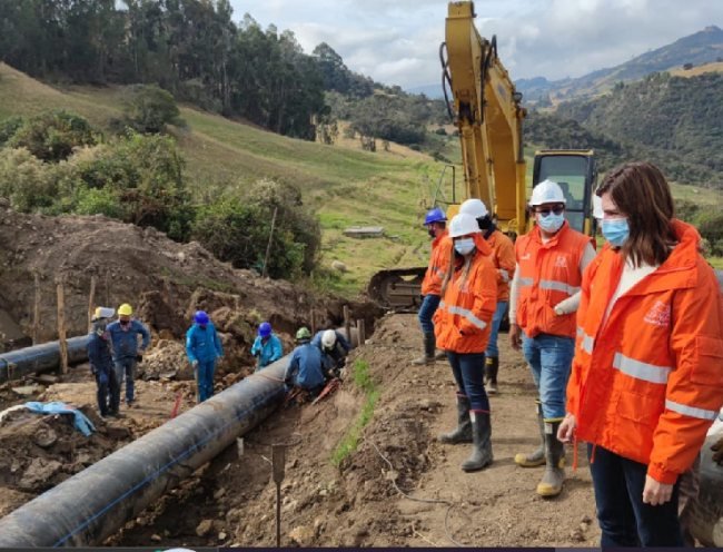 Trabajadores con cascos y chalecos naranjas supervisan la instalación de tuberías en una obra de construcción