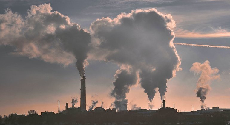 Humo y gases industriales saliendo de chimeneas de una planta contra un cielo al atardecer