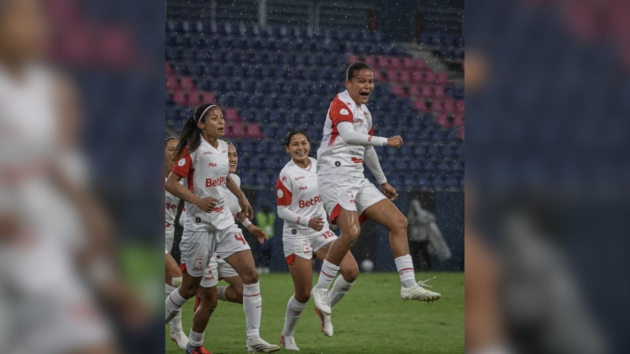 Jugadoras de fútbol con uniformes blancos celebran un gol en un campo de césped bajo la lluvia
