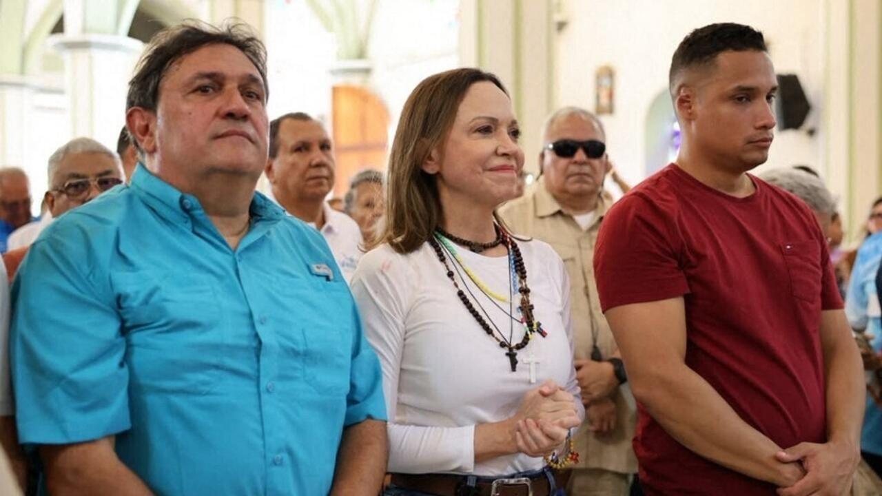 Tres personas de pie en un espacio público con otros asistentes al fondo