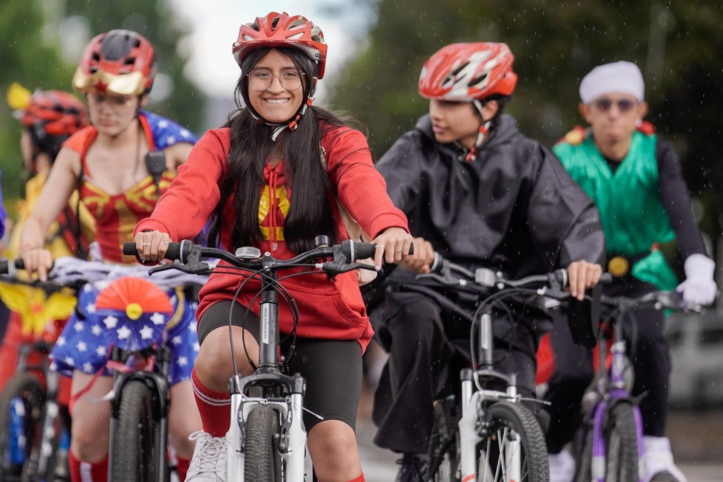 Personas con cascos y ropa deportiva pedalean en bicicletas por una vía bajo la lluvia