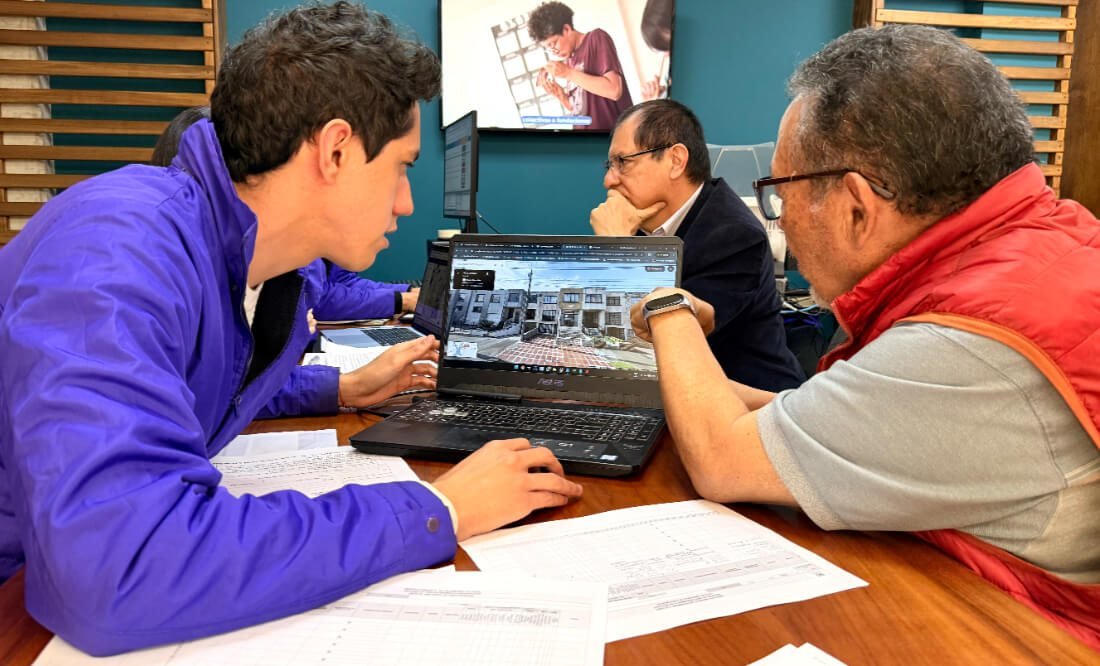 Dos hombres revisan un computador portátil con planos arquitectónicos en una oficina