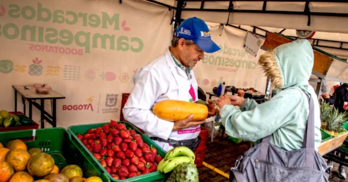 Un vendedor en un mercado de Bogotá sostiene un zapallo mientras interactúa con una cliente.