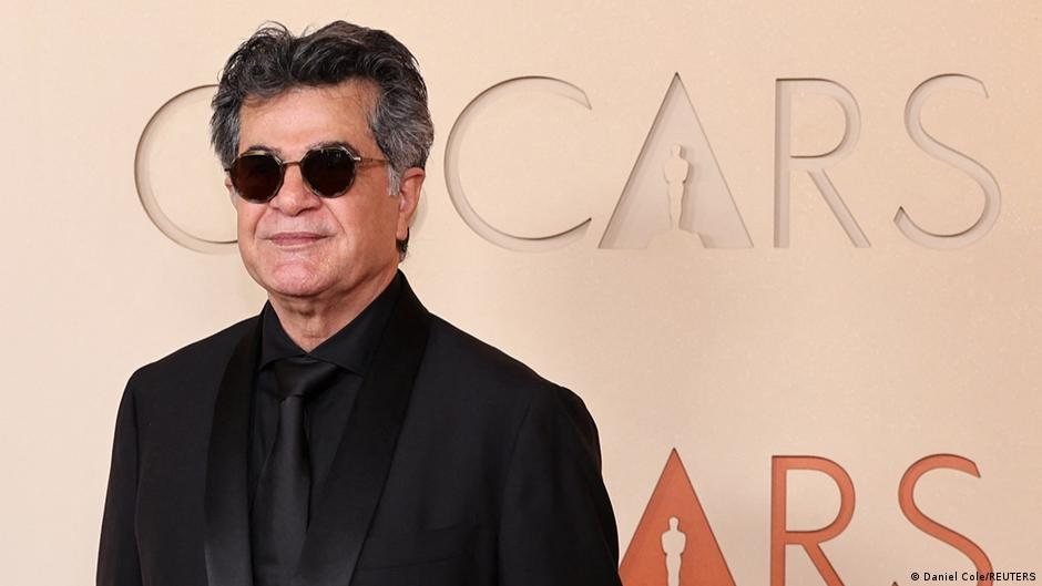 Hombre con gafas de sol y traje negro posa frente a un fondo con el logo de los Premios Oscar