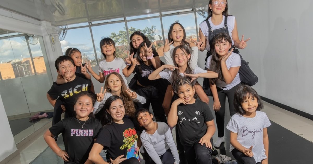Un grupo de niños y adultos posan sonrientes y haciendo señas de victoria frente a un ventanal.