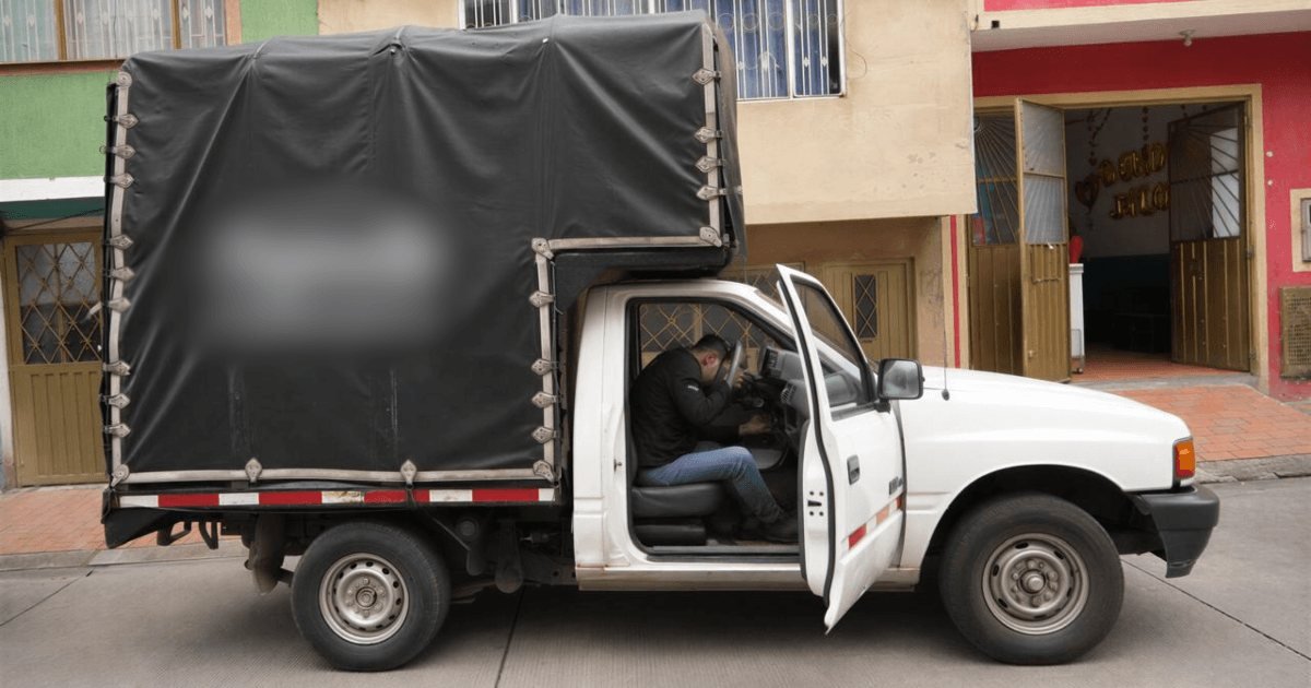 Un hombre sentado en la cabina de una camioneta de carga blanca con una estructura de lona negra.