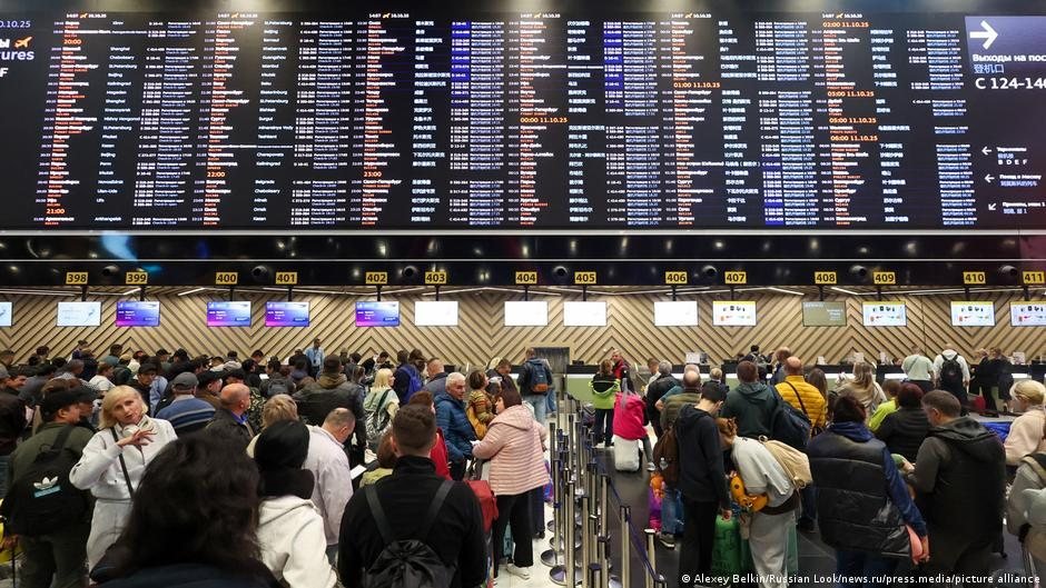 Vista de una terminal de aeropuerto con una gran pantalla de salidas y pasajeros caminando por el pasillo