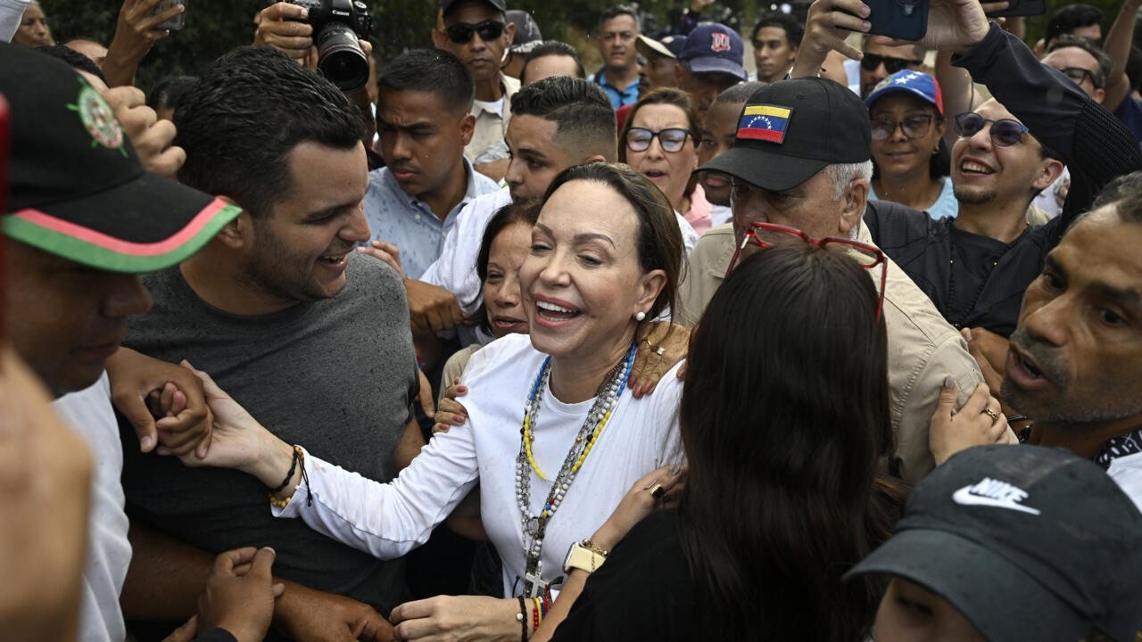 Una mujer sonriente rodeada de personas en un evento público con cámaras y teléfonos móviles