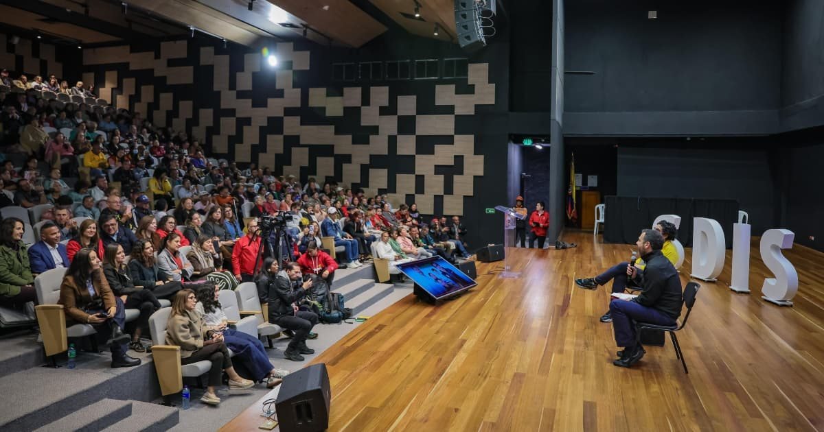 Un hombre sentado en un escenario frente a una audiencia numerosa en un auditorio moderno.