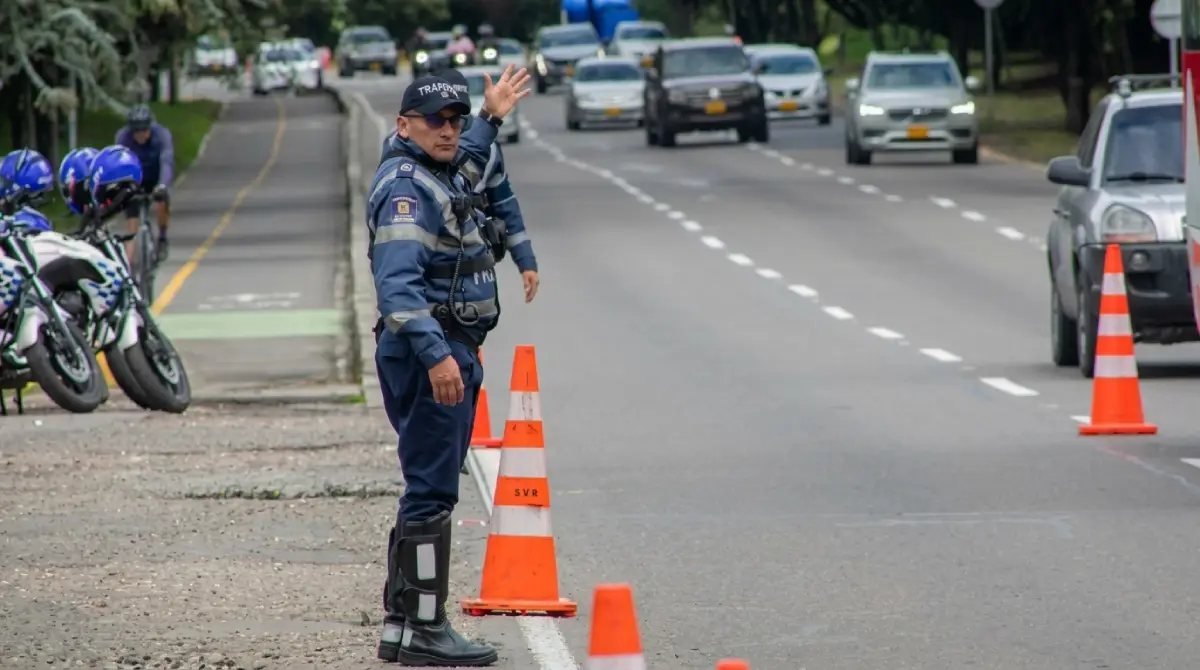 Un agente de tránsito con uniforme azul dirige el flujo vehicular en una avenida con conos naranjas