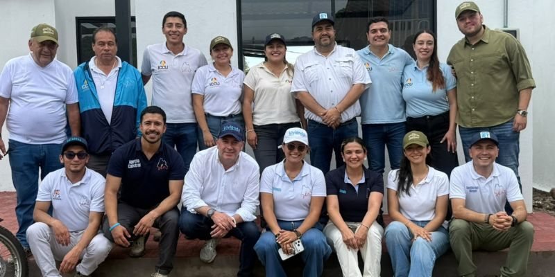 Un grupo de personas posan juntas frente a un edificio, algunas de pie y otras sentadas en el suelo