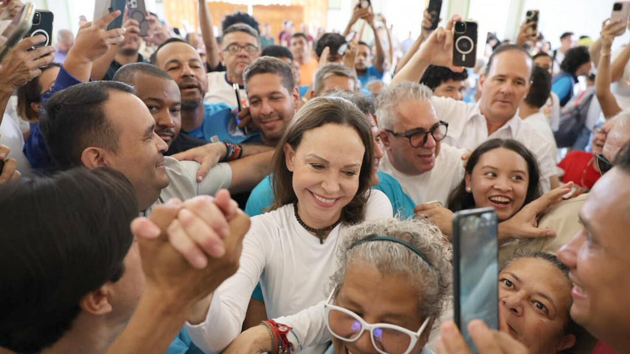 Una mujer sonriente rodeada de una multitud de personas que le toman fotografías con sus teléfonos móviles