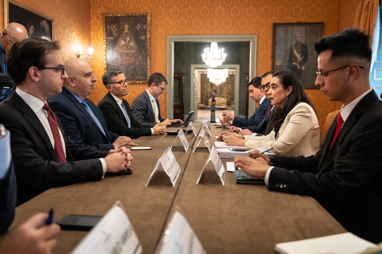 Delegaciones de Colombia y Estados Unidos se sientan a una mesa larga en una sala con paredes decoradas