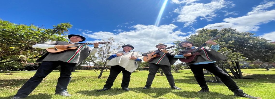 Cuatro músicos vestidos con trajes típicos de campesinos tocan instrumentos de cuerda en un parque bajo un cielo despejado