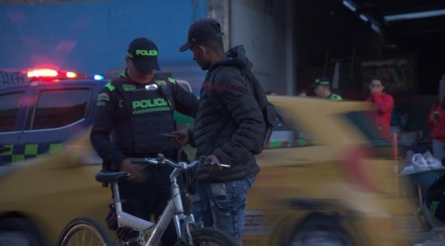 Un policía y un hombre con mochila frente a un taxi amarillo en una calle de noche