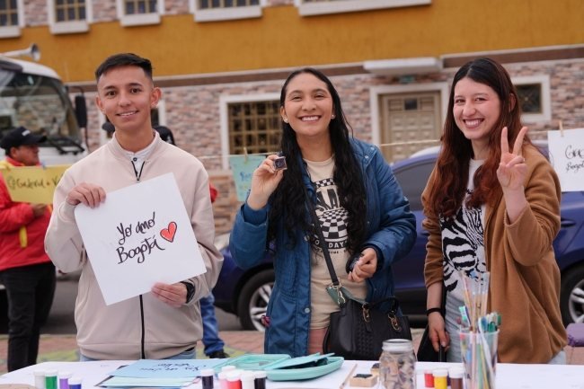 Tres personas sonríen frente a un puesto de actividades en una calle de Bogotá